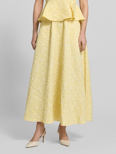 Modelka nosi Ausgestellter Maxi-Rock mit Strukturmuster Modell 'FIONA' von Vero Moda, żółty piqué jacquard, krój regular fit, długość maxi, strukturalna faktura, uni kolor, elastyczny pas, boczne kieszenie, widok całej sylwetki z przodu.
