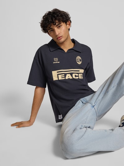 Männermodel trägt Regular Fit Poloshirt aus Waffel-Piqué Modell 'Peace' von ANOTHER COTTON LAB in Dunkelblau mit Label-Print, Nahaufnahme Oberkörper. Baumwoll-Mix, V-Ausschnitt, Rückenlänge Größe M 72 cm.
