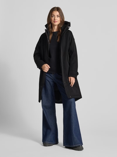 Modelka nosi czarną parkę 'Parka mit Kapuze und Thermore Füllung' od Didriksons, prosty krój, kaptur, wyhaftowane logo, boczne kieszenie z patką, zamek błyskawiczny, guziki i rzep, zakończenia rękawów z dzianiny, wiatroszczelny, wodoszczelny (10.000mm), oddychający, wypełnienie thermore, długość tyłu w rozmiarze 36: 102 cm, szerokość ramion w rozmiarze 36: 40 cm, szerokość w rozmiarze 36: 56 cm, długość rękawów w rozmiarze 36: 60 cm; neutralne tło, widok całej sylwetki z przodu.