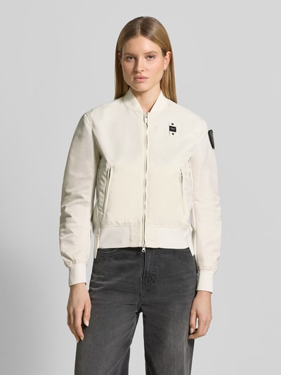 Frauenmodel trägt Bomberjacke mit Reißverschlusstaschen Modell 'LAURIE' von Blauer Usa in Creme mit gerippten Abschlüssen, Ganzkörperansicht von vorne. Loose Fit, Stehkragen, Label-Patches, Zweiwege-Reißverschluss, seitliche Taschen, glatte Textur.