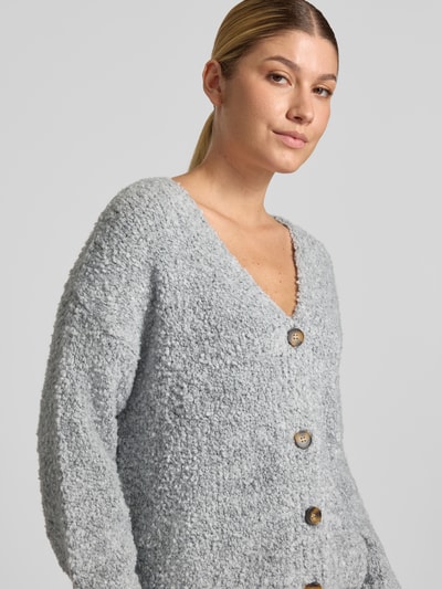 Frauenmodel trägt Cardigan mit V-Ausschnitt Modell 'So44fia' von ZABAIONE aus grauem Material-Mix, Knopfleiste, Nahaufnahme Oberkörper. Material-Mix mit Viskose-Anteil, gerader Schnitt, Rückenlänge 56 cm, Ärmellänge 47 cm.