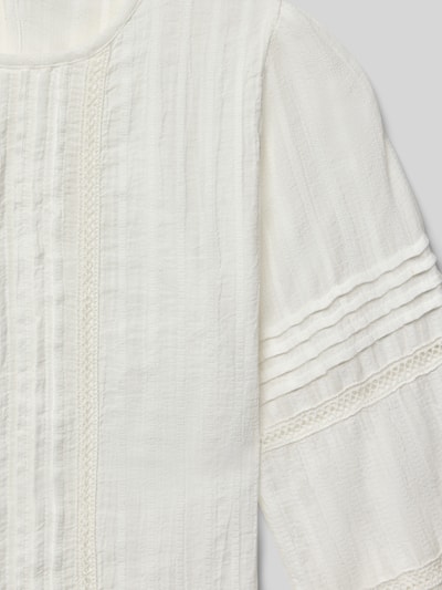 Mädchen trägt Blusenshirt mit Rundhalsausschnitt von Mango aus reiner Baumwolle, lockerer Schnitt, Raffungen, Nahaufnahme Oberkörper.
