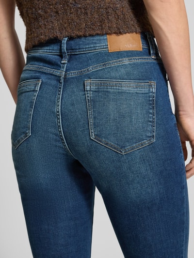 Frauenmodel trägt Slim Fit Jeans aus Baumwoll-Mix Modell 'BETSY' von s.Oliver RED LABEL in klassischem blauen Denim, Kontrastnähte, Mid Waist, Label Patch, Detailaufnahme Rückansicht.