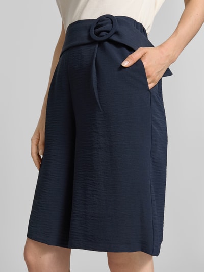 Vrouwenmodel draagt Straight Fit bermuda met siergesp van Zero in donkerblauw, bandplooien, achterzakken, deels elastische band, binnenbeenlengte 55 cm bij maat 36, bandwijdte 36 cm bij maat 36, detailopname heuppartij.