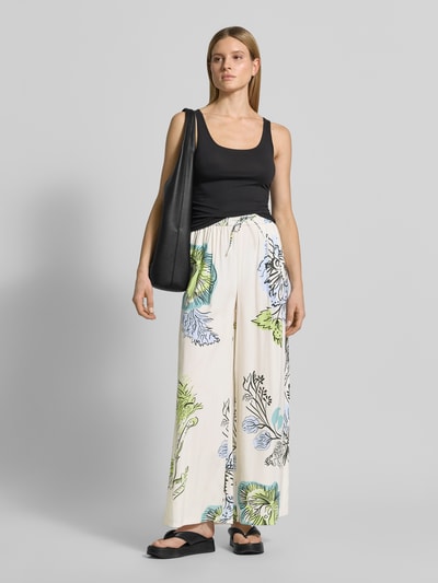 Frauenmodel trägt Stoffhose aus Seide-Mix von HERZENS mit floralem Muster, Loose-Fit, elastischer Bund, Tunnelzug, Ganzkörperansicht von vorne. Bundweite bei Größe 36: 37 cm, Innenbeinlänge: 76 cm.