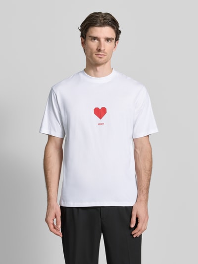 Männermodel trägt Regular Fit T-Shirt aus reiner Baumwolle Modell 'DALENTIN' von HUGO in Weiß mit rotem Motiv-Print, ganzkörperansicht von vorne.