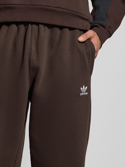 Mannenmodel draagt Straight Fit Sweatpants met Logo-Stitching van adidas Originals, bruine katoen, elastische taille, detailopname heup.