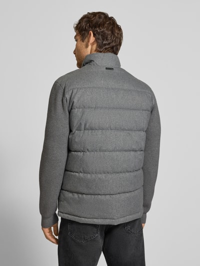 Männermodel trägt Steppjacke mit Stehkragen und Zweiwege-Reißverschluss von Christian Berg Men in Grau, Regular Fit, Ganzkörperansicht Rückansicht. Kontext: Reißverschlusstaschen, Rückenlänge 70 cm, Schulterbreite 51 cm, Brustweite 60 cm, Ärmellänge 69 cm.