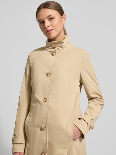 Frauenmodel trägt Trenchcoat mit Stehkragen und Ärmelriegeln von Christian Berg Woman Selection in Beige, glatte Textur, Nahaufnahme Oberkörper.