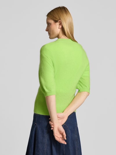 Frauenmodel trägt Strickjacke aus Kaschmir-Baumwoll-Mix mit 1/2-Arm von HERZENS in Neon-Grün, Regular Fit, Rundhalsausschnitt, Knopfleiste, Rückenlänge 58 cm, Ärmellänge 31 cm, glatte Textur, kombiniert mit dunkelblauem Rock, Ganzkörperansicht Rückansicht.