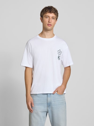 Männermodel trägt Relaxed Fit T-Shirt aus reiner Baumwolle Modell "DYLAN" von JACK & JONES in Weiß mit Print-Detail, Nahaufnahme Oberkörper.