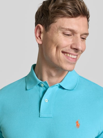 Männermodel trägt Regular Fit Poloshirt aus reine katoen van Polo Ralph Lauren in effen turquoise, piquéstructuur, logo-detail, korte knoopsluiting, polokraag, korte mouw, geribde zoom, detailopname bovenlichaam.