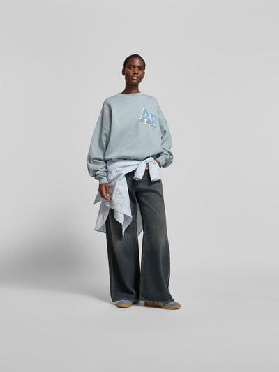 Frauenmodel trägt Oversized Sweatshirt aus reiner Baumwolle von Anine Bing in hellem Blau mit Label-Detail, Elastische Abschlüsse, Rundhalsausschnitt, Rückenlänge 64 cm bei Größe S, Ganzkörperansicht von vorne.