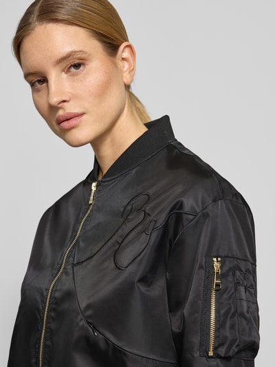 Kobiece model nosi bomberka 'Bomberjacke mit Zweiwege-Reißverschluss' od Original Bombers, czarny kolor, haft, krój regular fit, stójka, kieszenie zapinane na zamek błyskawiczny, zamek błyskawiczny dwustronny, zbliżenie na górną część ciała