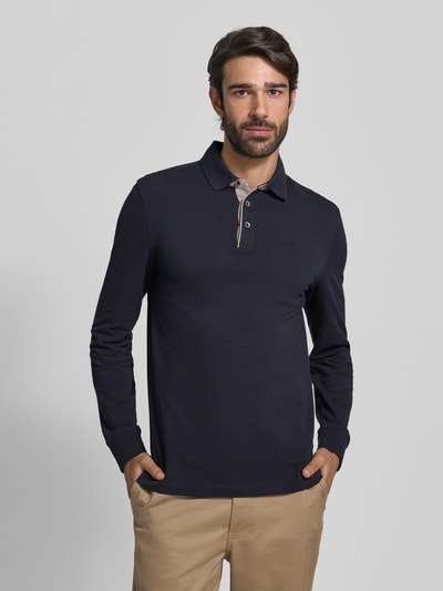 Męski model nosi Regular Fit Koszulkę polo z kołnierzykiem w kontrastowym kolorze i wyhaftowanym logo od Bugatti z bawełny, bluzka z długim rękawem, listwa guzikowa, kolor granatowy, długość tyłu przy rozmiarze M: 71 cm, widok na cały przód.