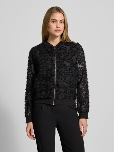 Frauenmodel trägt semitransparenten Blouson Modell 'Pi44nioa' von ZABAIONE in Schwarz mit Struktur, Slim Fit, Ganzkörperansicht von vorne. Damen Blouson, Stehkragen, Reißverschluss, Rückenlänge 56 cm, Schulterbreite 45 cm, Brustweite 51 cm, Ärmellänge 59 cm.