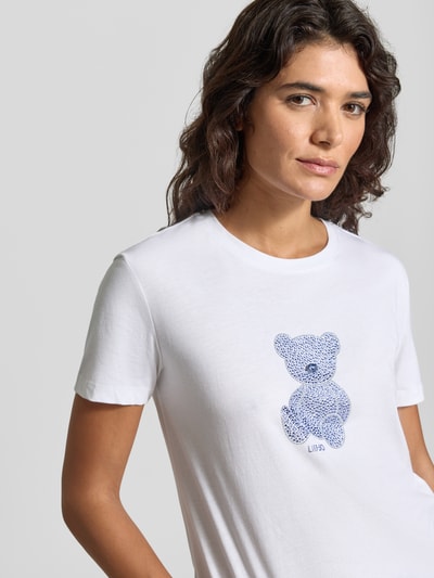 Kobieta nosi Slim Fit T-Shirt mit Ziersteinbesatz von Liu Jo White, damski t-shirt, bawełna, motyw, okrągły dekolt, długość tyłu w rozmiarze S: 57 cm, zbliżenie na górną część ciała.