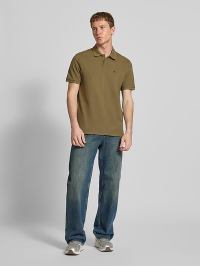 Männermodel trägt Straight Fit Poloshirt mit Label-Stitching von Calvin Klein Jeans aus reiner Baumwolle, Polokragen, gerippte Ärmelabschlüsse, olivgrün, Rückenlänge 71 cm bei Größe M, Ganzkörperansicht von vorne.