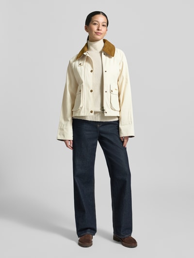 Modelka nosi Regular Fit Parka aus reiner Baumwolle von Barbour, efekt: jednolity kolor, krój regular fit, wykładany kołnierz, zapięcie na ukryty zamek błyskawiczny i listwę z zatrzaskami, aplikacja z wyhaftowanym logo, rękawy długi, kieszenie z patką i kieszeń wewnętrzna, materiał: czysta bawełna; jasny, kremowy kolor, proste linie, gładka struktura, widoczne tekstury materiału. Ganzkörperansicht von vorne.
