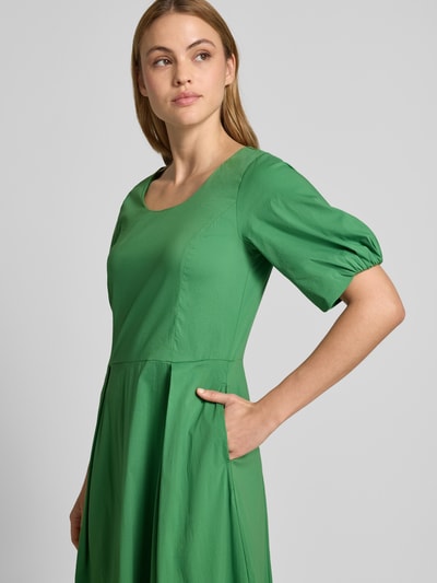 Vrouwenmodel draagt Midikleid mit Raffungen van More & More in groen katoenmix met getailleerde pasvorm en stolpplooien, nahaufnahme bovenlichaam. Context: dames midi-jurk van More & More, elastische katoenmix, getailleerd, ronde hals, stolpplooi, halflange mouwen, plooien, ruglengte maat 36: 119 cm, borstwijdte maat 36: 44 cm, mouwlengte maat 36: 29 cm.