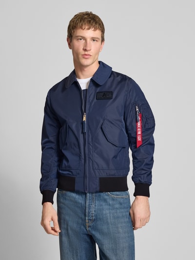 Männermodel trägt Regular Fit Bomberjacke mit Logo-Patch von Alpha Industries in Dunkelblau, Umlegekragen, aufgesetzte Taschen, Reißverschluss, elastische Abschlüsse, Ganzkörperansicht von vorne. Rückenlänge bei Größe M: 66 cm, Schulterbreite 44 cm, Brustweite 56 cm, Ärmellänge 66 cm.