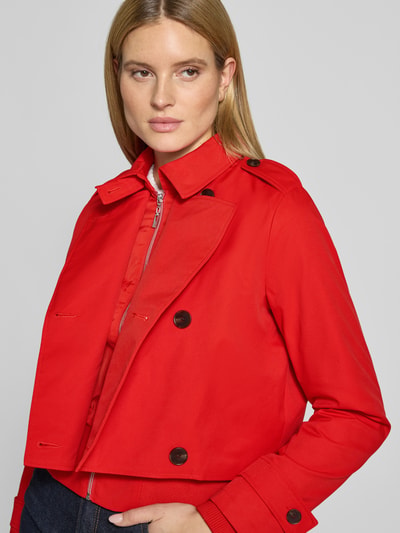 Vrouwenmodel draagt 'Trenchcoat mit Ärmelriegeln' van monari in regular fit, rood, dubbele rij knopen, reverskraag, detailopname bovenlichaam.