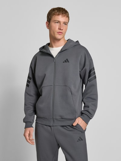 Männermodel trägt Sweatjacke mit Kapuze von adidas Sportswear in Grau, Baumwoll-Materialmix, Reißverschluss, Label-Print, Ganzkörperansicht von vorne.
