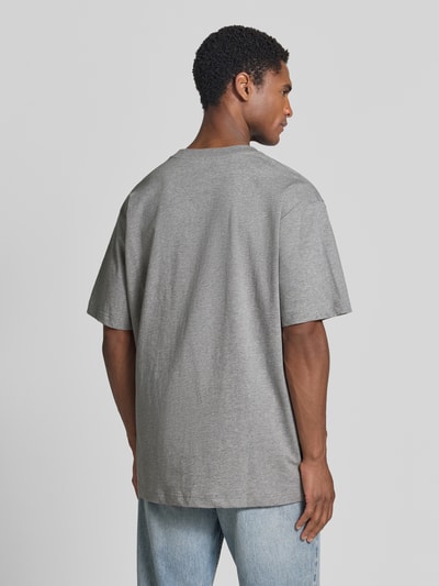 Męskil model nosi szarą koszulkę o kroju oversized, model 'ICONIC Å MAARKOS' od ARMEDANGELS, koszulka Herren Oversized Shirt, całopostaciowy widok z tyłu.