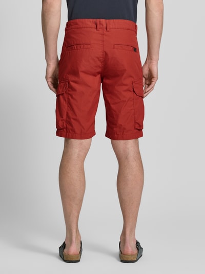 Mannenmodel draagt Bermudas met Cargozakken van camel active in rood, puur katoen, regular fit, steekzakken, labeldetail, binnenbeenlengte 26 cm, bandwijdte maat 32 is 44 cm. Volledige lichaamsaanzicht achteraan.