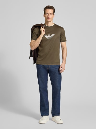 Männermodel trägt Regular Fit T-Shirt mit Logo-Stitching von Emporio Armani in Olivgrün und Jeans, Rundhalsausschnitt, Ganzkörperansicht von vorne.