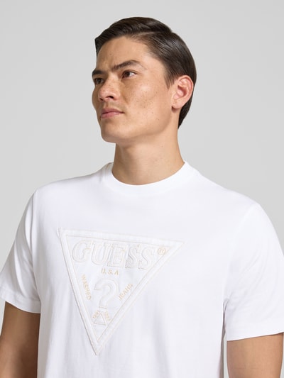 Mannenmodel draagt T-shirt met logo en ronde hals van guess, puur katoen, regular fit, ruglengte maat M 70 cm, nahaufnahme bovenlichaam.