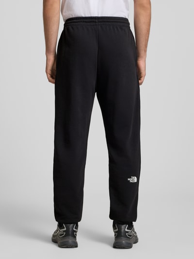 Männermodel trägt Sweatpants mit Logo-Print von The North Face aus Baumwoll-Mix, Slim-Fit, elastischer Bund mit Kordelzug, Innenbeinlänge 70 cm, schwarze Farbe, elastische Abschlüsse, Ganzkörperansicht Rückansicht.