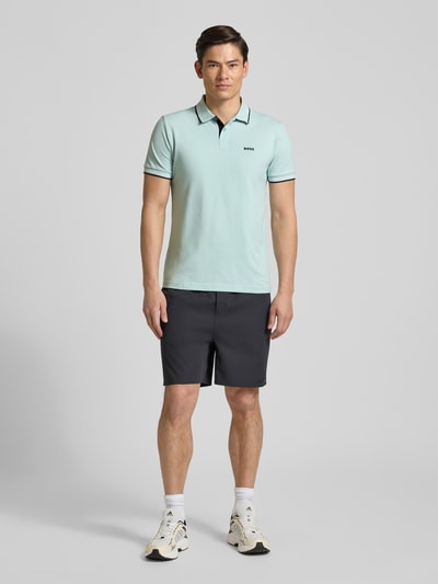 Männermodel trägt Slim Fit Poloshirt aus reiner Baumwolle Modell 'PAUL' von BOSS Green, hellgrün, unifarben, Ganzkörperansicht von vorne.
