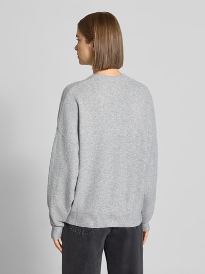 Modelka nosi sweter z dzianiny 'Strickpullover mit Label-Print' od REVIEW, luźny krój, okrągły dekolt, nadruk z logo, bardzo szerokie ramiona, prążkowany dół, długość tyłu w rozmiarze S: 56 cm, długość rękawa w rozmiarze S: 44 cm, szary melanż, miękka faktura; widok całej sylwetki od tyłu.
