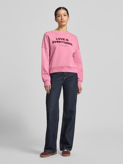 Frauenmodel trägt Regular Fit Sweatshirt aus reiner Baumwolle von Tom Tailor Denim in Rosa, unifarben, mit Rundhalsausschnitt und Label-Schriftzug, ganzkörperansicht von vorne.