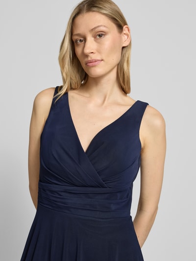 Frauenmodel trägt Cocktailkleid in Wickel-Optik mit V-Ausschnitt von TROYDEN COLLECTION, dunkelblauer Mesh, taillierter Schnitt, Drapierungen, Nahaufnahme Oberkörper. Kontext: Damen Cocktailkleid, Midikleid, Rückenlänge bei Größe 36: 108 cm, Brustweite bei Größe 36: 41 cm.
