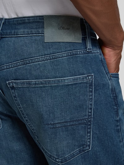 Männermodel trägt Tapered Fit Jeans aus Baumwoll-Mix von s.Oliver RED LABEL, mittleres Blau, sichtbare Struktur, Nahaufnahme Rückansicht.