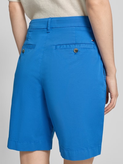 Frauenmodel trägt Regular Fit Chino-Shorts aus Baumwoll-Lyocell-Mix von Tommy Hilfiger, efekt: jednolity kolor, wyhaftowane logo, wpuszczane kieszenie, kieszenie z tyłu, mieszanka bawełny i lyocellu, zapięcie na guzik i zamek błyskawiczny, krój regular fit, Ganzkörperansicht Rückansicht.