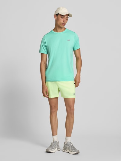 Männermodel trägt Funktionsshirt mit Rundhalsausschnitt und Logo von New Balance in Mintgrün, Regular-Fit, Ganzkörperansicht von vorne. Rückenlänge bei Größe M: 69 cm.