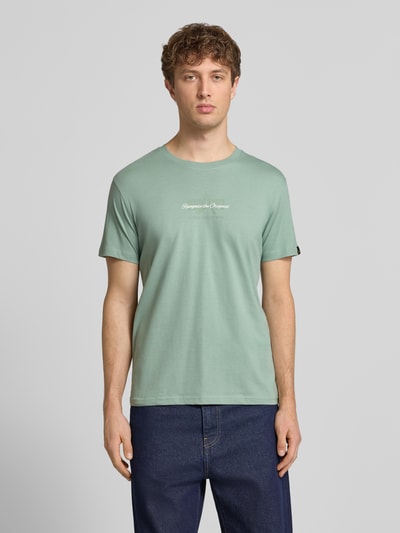 Männermodel trägt T-Shirt mit Label-Detail von Alpha Industries in Mint, Reine Baumwolle, Gerader-Schnitt, Rundhalsausschnitt, Rückenlänge 68 cm, Ganzkörperansicht von vorne.