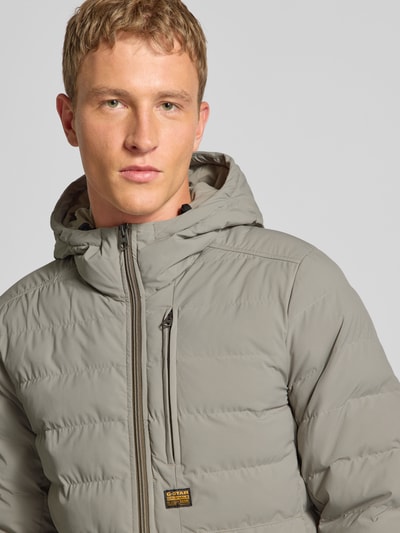 Männermodel trägt Steppjacke mit Brusttasche und Label-Detail Modell 'Foundation' von G-Star, Nahaufnahme Oberkörper, Regular-Fit, Kapuze, Reißverschluss, dezentes Grau, glatte Textur, Kontext: Herren Steppjacke, Rückenlänge 70 cm, Schulterbreite 46 cm, Brustweite 56 cm, Ärmellänge 70 cm.