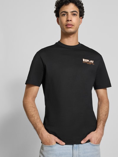 Męski model nosi Regular Fit T-Shirt mit Logo-Stitching od Replay, czarny, bawełna, nadruk z napisem, okrągły dekolt, długość tyłu w rozmiarze M 70 cm, widok na górną część ciała z przodu.