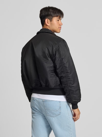 Männermodel trägt schwarze Bomberjacke mit seitlichen Pattentaschen und Label-Patch von Alpha Industries, Rückansicht, Regular Fit.