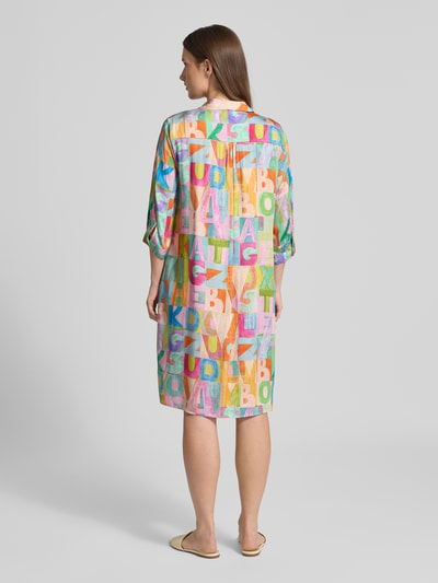 Männermodel trägt Relaxed Fit Hemdblusenkleid aus reiner Viskose von Milano Italy, kolorowy wzór liter, krój relaxed fit, długość tyłu 97 cm, szerokość w rozmiarze 36: 48 cm, 3/4 rękaw, widok całej sylwetki z tyłu.