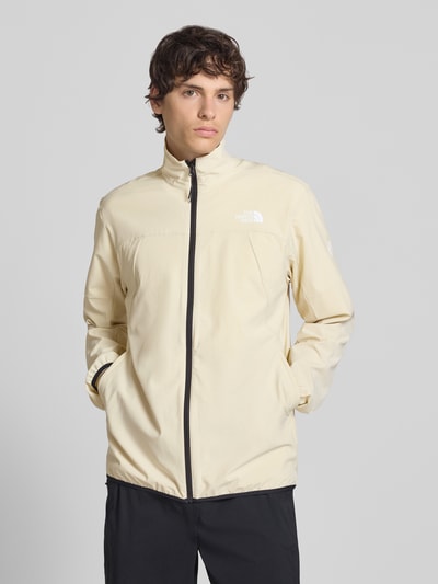 Männermodel trägt Regular Fit Jacke mit Stehkragen Modell 'Mountain' von The North Face in Beige mit schwarzem Reißverschluss, Logo-Print, elastischem Material-Mix, Ganzkörperansicht von vorne.