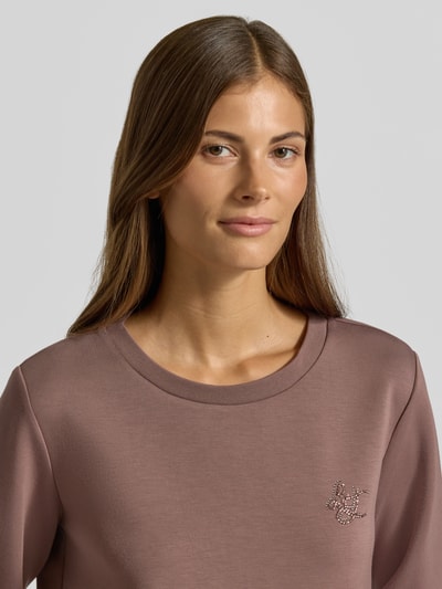 Vrouwenmodel draagt relaxed fit sweatshirt uit viscosemix Model 'Felpa' van Liu Jo met siersteentjes en elastische boordjes, close-up bovenlichaam.