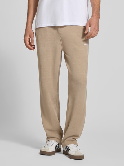 Männermodel trägt Wide Fit Sweatpants mit Label-Detail Modell 'Mezzano' von PEGADOR in Beige mit elastischem Bund, Eingrifftaschen, Ganzkörperansicht von vorne.