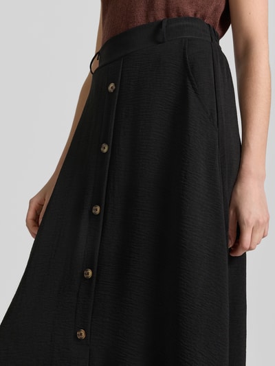 Frauenmodel trägt Midirock mit Knopfleiste Modell 'Cath' von Soyaconcept in Schwarz, strukturierte Textur, Nahaufnahme Oberkörper. Leichte A-Linie und Gürtelschlaufen, Bundweite 36 cm, Gesamtlänge 90 cm.