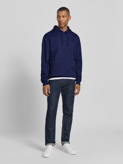 Männermodel trägt Oversized Hoodie mit Logo-Stitching von GAP aus Baumwoll-Mix in Dunkelblau mit Känguru-Tasche, Ganzkörperansicht von vorne.