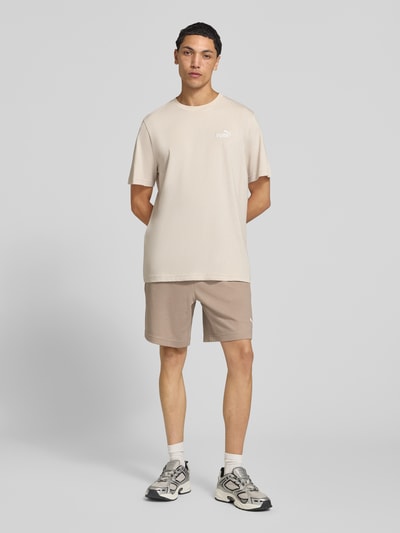 Männermodel trägt Relaxed Fit Sweatshorts aus Baumwoll-Mix 'ESS ELEVATED' von PUMA in Beige, glatte Textur, Herren Sweatshorts von PUMA Performance, Ganzkörperansicht von vorne.